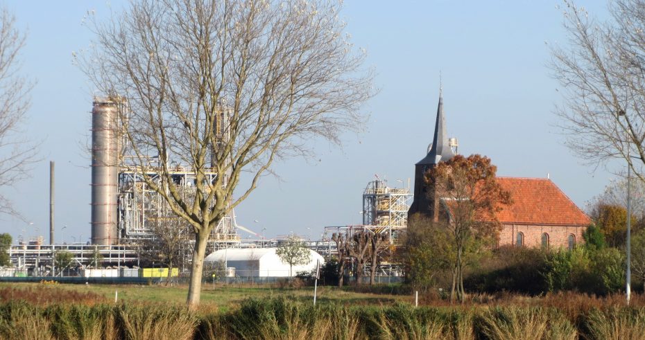 Het kerkje van Heveskes staat eenzaam tussen grijze fabrieken, stomende buizen en rokende schoorstenen